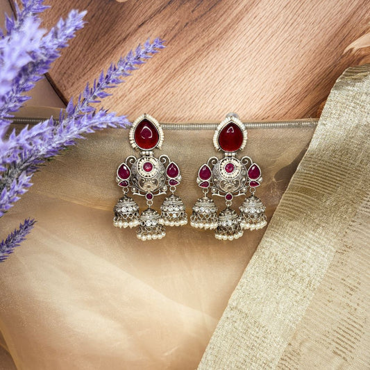 Ornate silver earrings with red gemstones on a fabric background